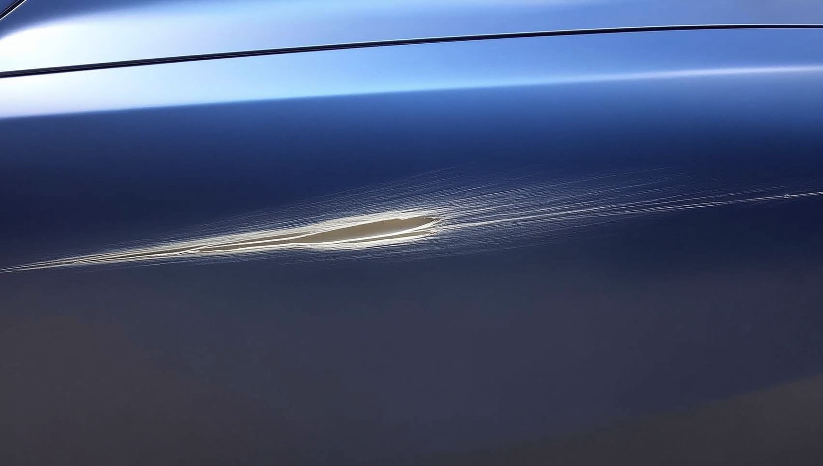 Deep scratch on a dark blue car door panel exposing the light gray primer layer beneath the paint (illustrative image)
