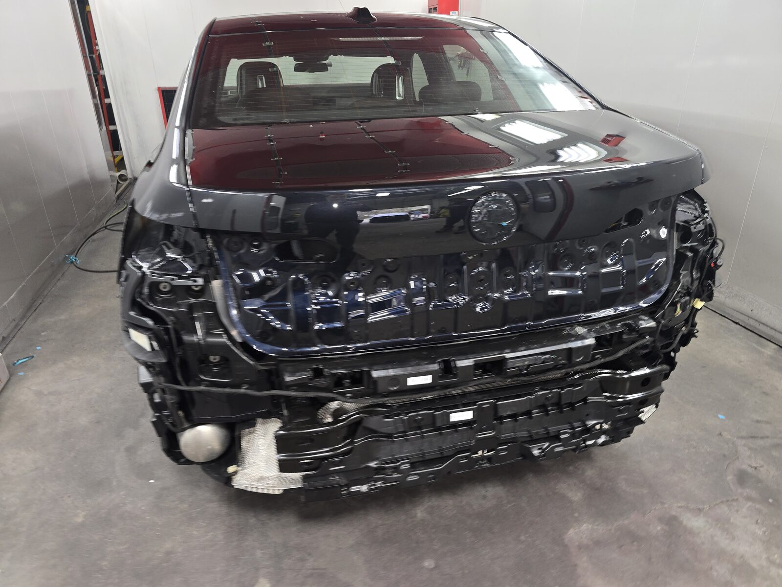 Black sedan in the shop with rear bumper and trim removed for repair