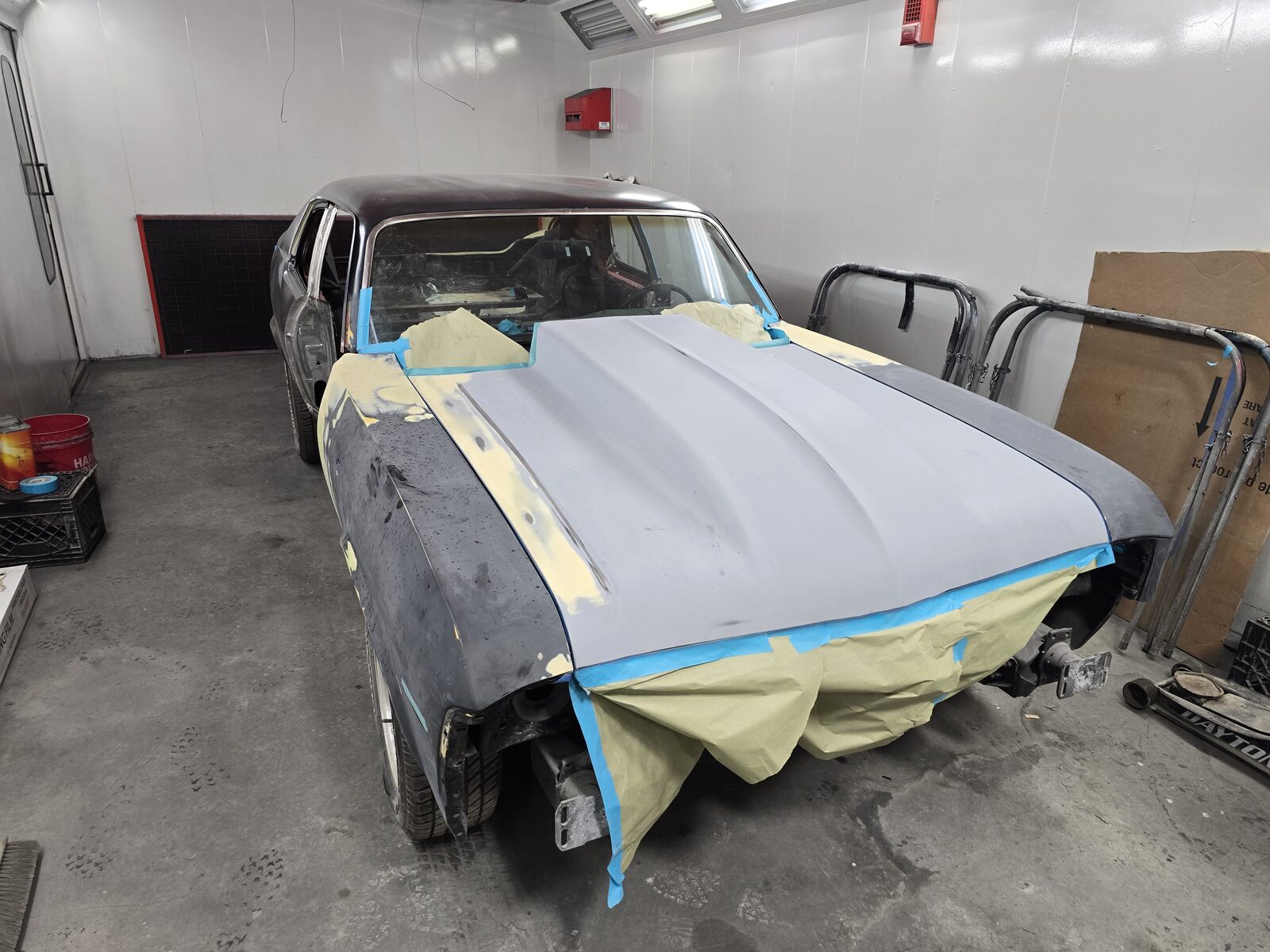Classic coupe masked in the paint booth with its hood in gray primer