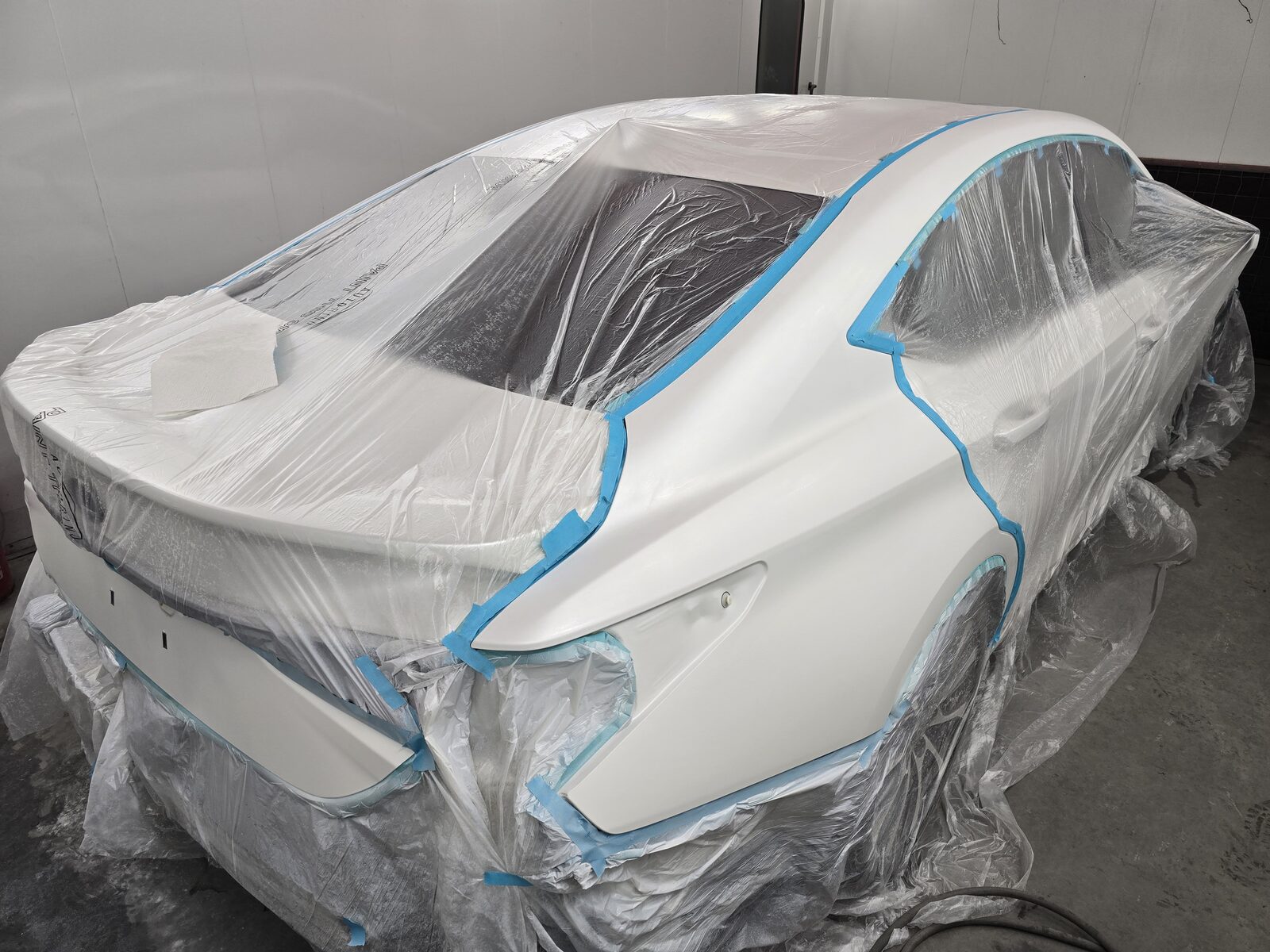 White sedan masked off in the spray booth with fresh paint