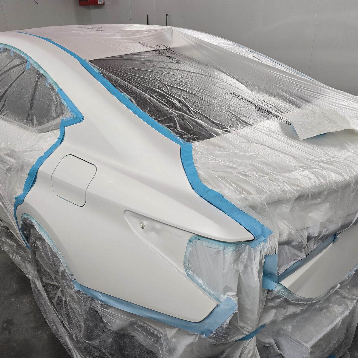 Freshly painted sedan under masking in the spray booth